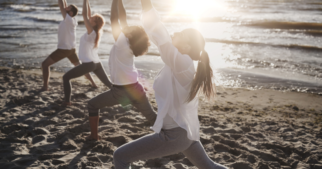 Four people on a beach practising yoga- a practice recommended to improve fertility when TTC. 